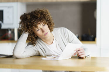 Thoughtful freelancer with note pad and smart phone leaning on desk - JSMF02713