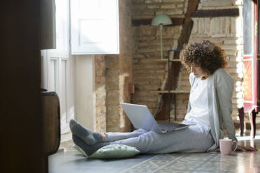 Freelancer sitting on floor and working through laptop at home - JSMF02716