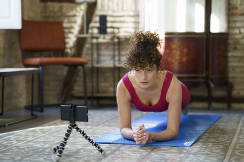 Frau mit Smartphone übt Yoga auf Matte zu Hause - JSMF02718