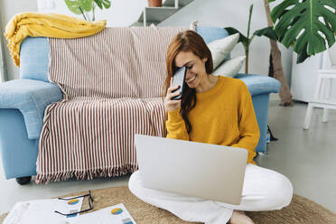 Happy woman with smart phone and laptop sitting on carpet at home - JJF00234
