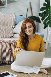 Happy woman with laptop sitting in living room at home - JJF00235