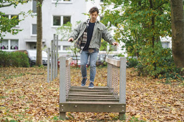 Young man walking on planks on playground - KNSF09676