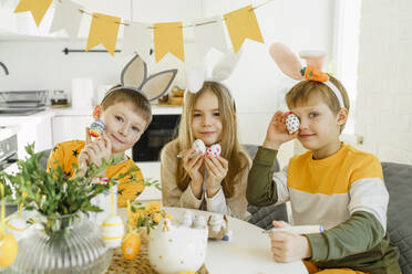 Fröhliche Jungen und Mädchen tragen Hasenohren-Stirnbänder und halten Ostereier zu Hause - VBUF00261