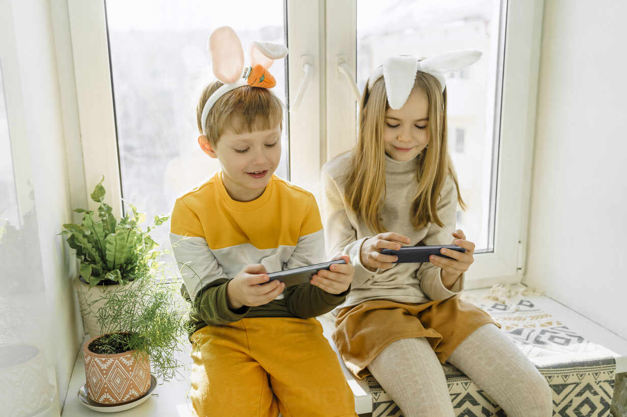 Happy girl and boy playing video games on smart phone at home stock photo