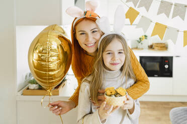 Glückliches Mädchen mit Mutter, die einen Luftballon hält, feiert Ostern zu Hause - VBUF00271