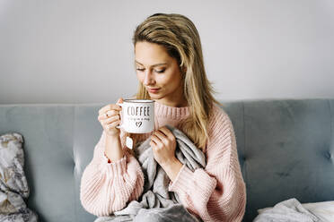 Smiling young woman drinking coffee sitting on sofa at home - JJF00242