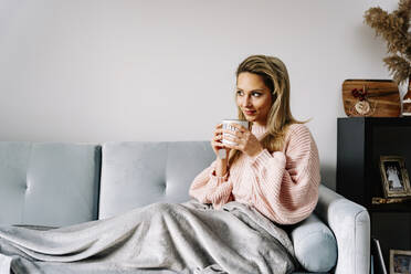 Junge Frau trinkt Kaffee auf dem Sofa zu Hause - JJF00247