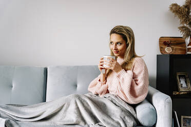 Young woman having coffee sitting on sofa at home - JJF00247