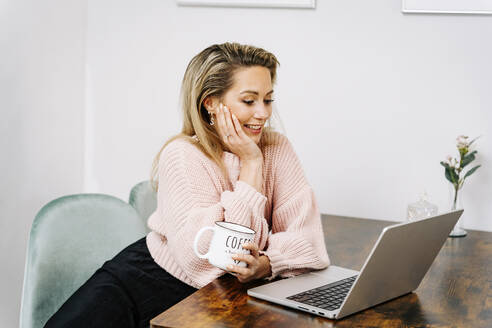 Glückliche Frau mit Kaffeetasse und Laptop zu Hause - JJF00260