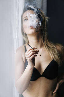 Sinnliche junge Frau beim Rauchen einer Zigarette zu Hause - JJF00269