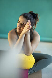 Thoughtful woman with hands clasped sitting on yoga mat - AXHF00265