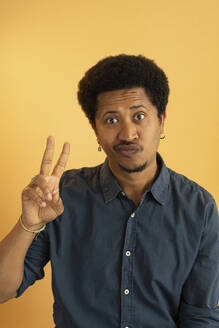 Man showing peace sign gesture against yellow background - AXHF00266