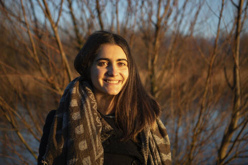 Happy young woman in front of tree and lake in sunlight - AXHF00268