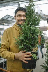 Happy man holding potted plant at store - ANAF01028