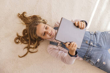 Happy girl using tablet PC lying on carpet at home - LJF02495