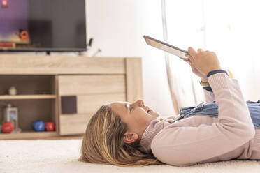 Lächelndes Mädchen mit Tablet-PC auf dem Teppich im Wohnzimmer zu Hause liegend - LJF02496