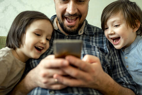 Glücklicher Vater, der sein Smartphone mit seinen Kindern zu Hause teilt - ANAF01030