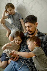 Father and sharing smart phone with kids on sofa at home - ANAF01033