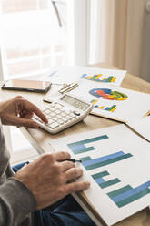 Hands of businessman examining graphs and doing calculations in office - MGRF00898