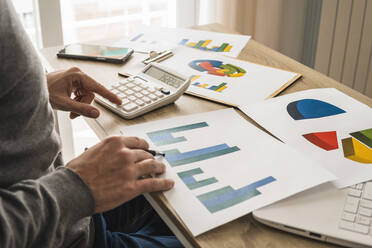 Businessman doing calculations with graphs at desk in office - MGRF00899