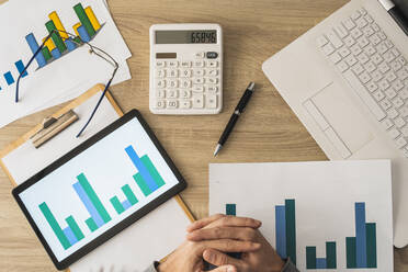 Hände eines Geschäftsmannes mit Taschenrechner und Diagrammen auf einem Tisch - MGRF00900