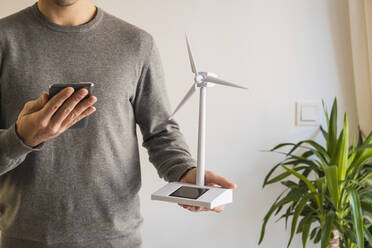 Geschäftsmann mit Windkraftanlage Modell mit Smartphone im Büro - MGRF00902