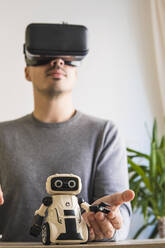 Businessman wearing VR glasses analyzing toy robot in office - MGRF00905