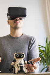 Geschäftsmann mit VR-Brille, der einen Spielzeugroboter im Büro analysiert - MGRF00905