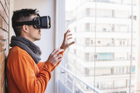 Geschäftsmann mit Virtual-Reality-Simulator gestikuliert in der Nähe des Fensters - MGRF00909