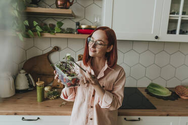 Smiling woman eating salad in kitchen at home - YTF00566