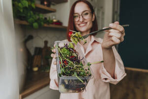 Woman showing fresh salad in kitchen at home - YTF00568