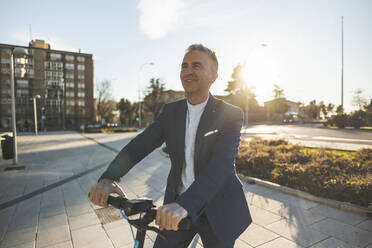 Happy businessman with push scooter standing at footpath - JCCMF09454