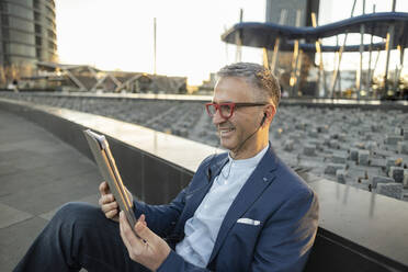 Happy businessman using tablet PC at office park - JCCMF09461