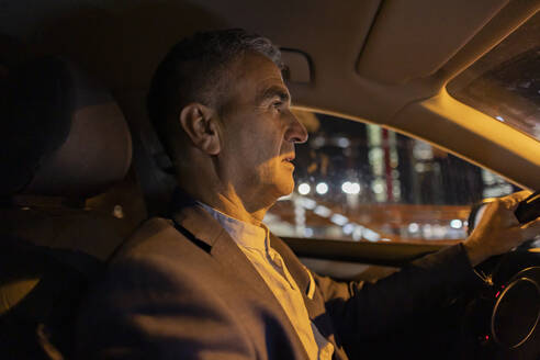 Businessman driving car at night - JCCMF09478