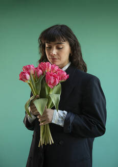 Young woman holding tulip flowers against green background - AXHF00270