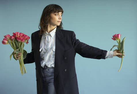 Woman holding tulip flowers against blue background - AXHF00272