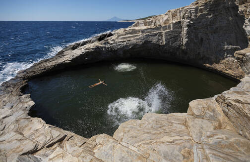 Woman swimming in cave pool on sunny day - AXHF00275