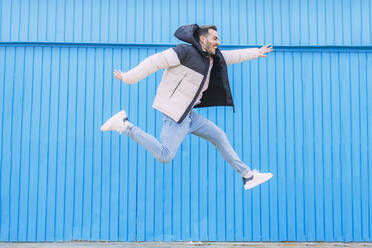 Fröhlicher Mann, der vor eine blaue Wand springt - EGHF00724