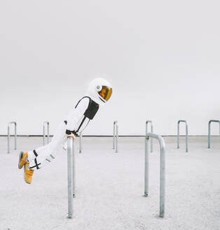 Boy wearing spacesuit leaning on bicycle rack - NDEF00348