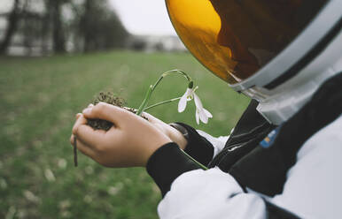 Junge mit Weltraumhelm hält Blume in der Natur - NDEF00349