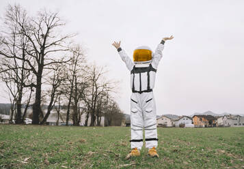 Boy wearing spacesuit standing with arms raised in nature - NDEF00351