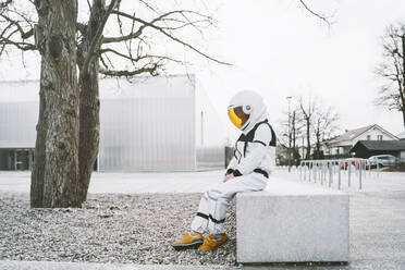 Junge im Astronautenkostüm sitzt auf einem Sitz am Fußweg - NDEF00353