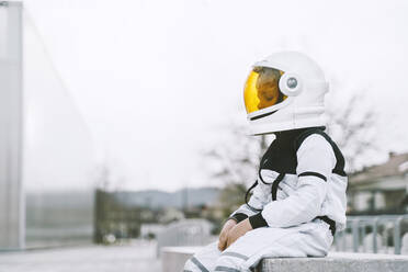Boy wearing astronaut costume sitting on seat - NDEF00354