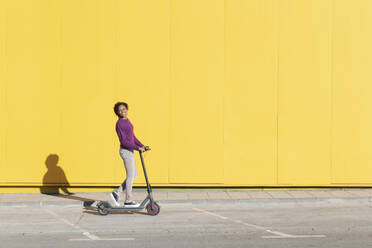 Woman riding electric scooter on footpath - LMCF00160