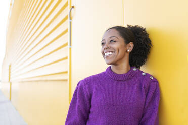 Thoughtful woman wearing purple sweater standing by yellow wall - LMCF00163