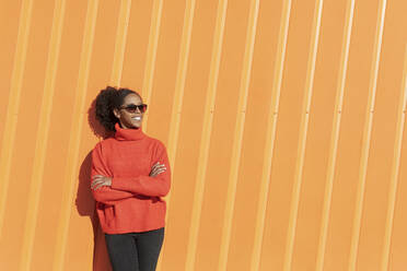 Glückliche Frau mit Sonnenbrille vor einer orangefarbenen Wand an einem sonnigen Tag - LMCF00168
