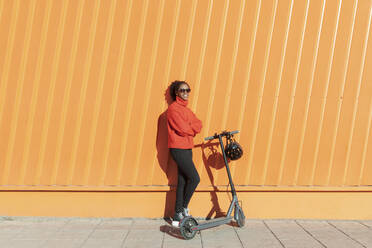 Frau mit Sonnenbrille und Elektroroller vor einer Mauer - LMCF00176