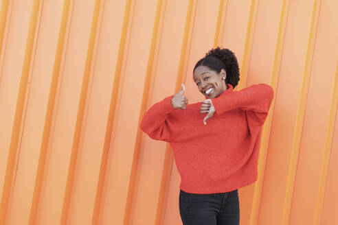 Glückliche Frau, die vor einer orangefarbenen Wand gestikuliert - LMCF00186