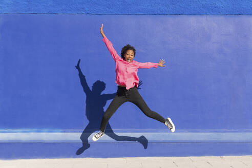 Unbekümmerte Frau, die auf dem Fußweg vor einer blauen Wand springt - LMCF00191