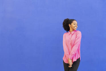 Glückliche Frau mit rosa Hemd vor blauer Wand - LMCF00194